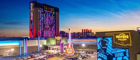 A Hard Rock Hotel & Casino in Tulsa with a large parking lot, a prominent guitar-shaped sign, and a building with vertical neon lights.