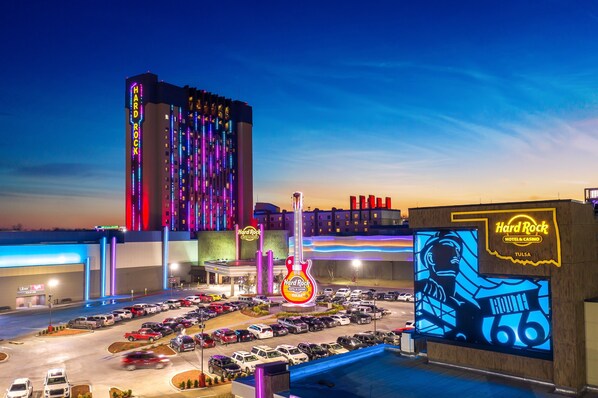 Un hotel casino Hard Rock & Casino en Tulsa con un amplio estacionamiento, un llamativo letrero con forma de guitarra y un edificio con luces de neón verticales.