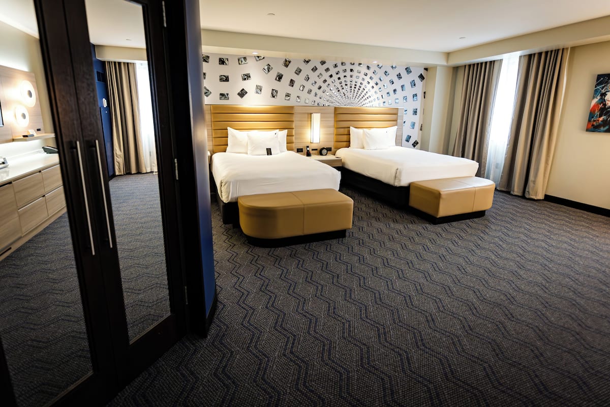 Habitación de hotel con dos camas, un espejo grande, un escritorio y piso alfombrado.