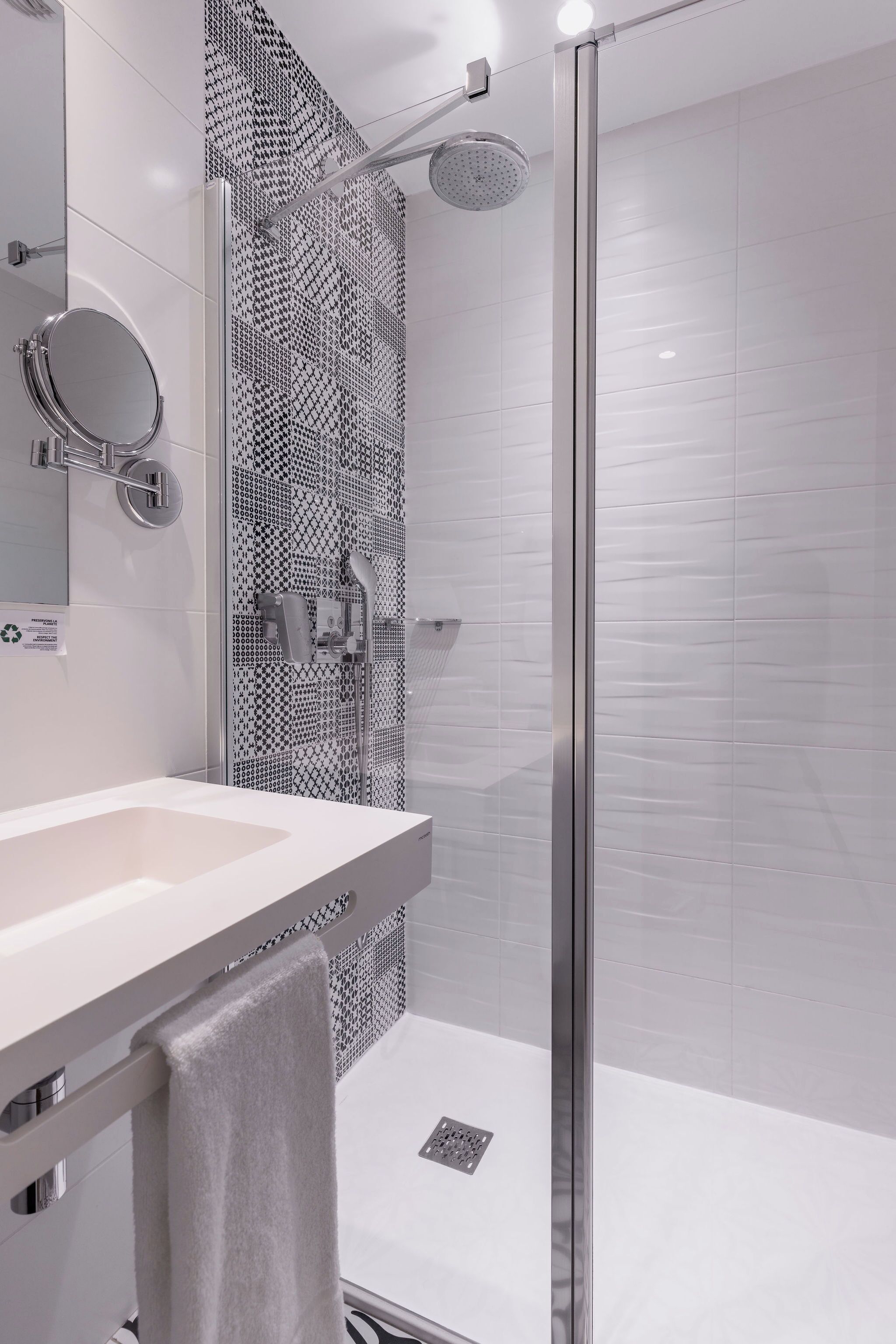 A modern bathroom with a glass shower enclosure, a white sink, and a patterned wall.