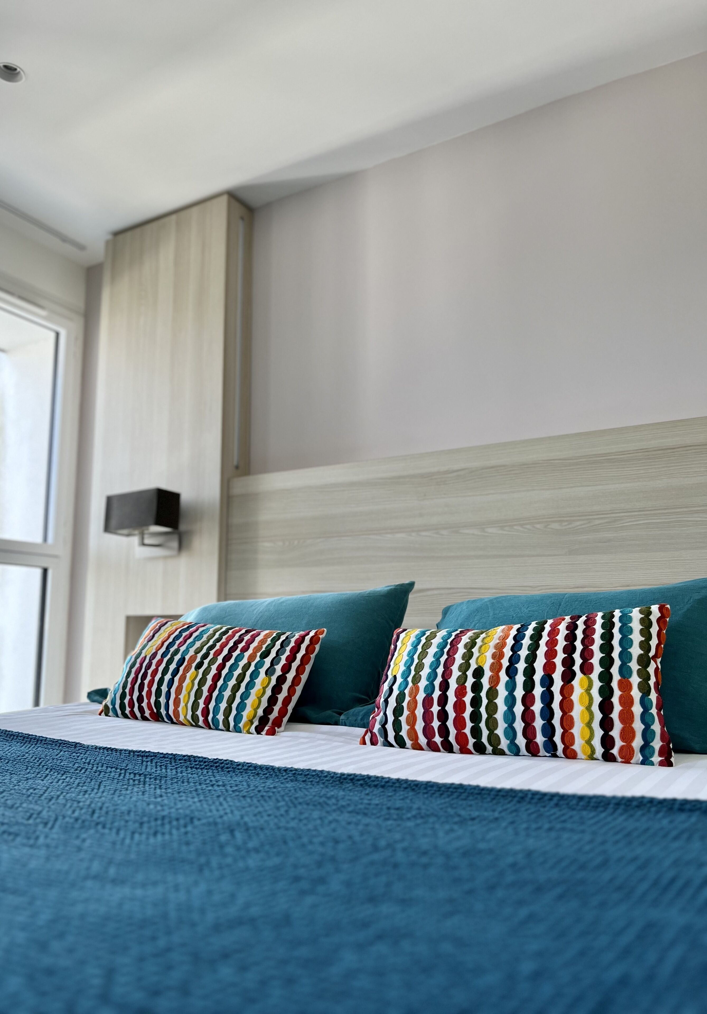Une chambre d’hôtel moderne avec un grand lit, une literie de couleur turquoise et des coussins à pois colorés.