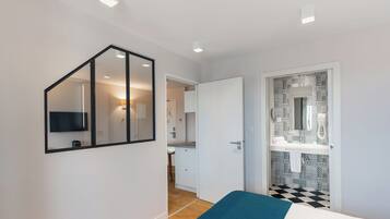 A modern bedroom with a bed, a TV mounted on the wall, and a bathroom with a patterned tile backsplash.