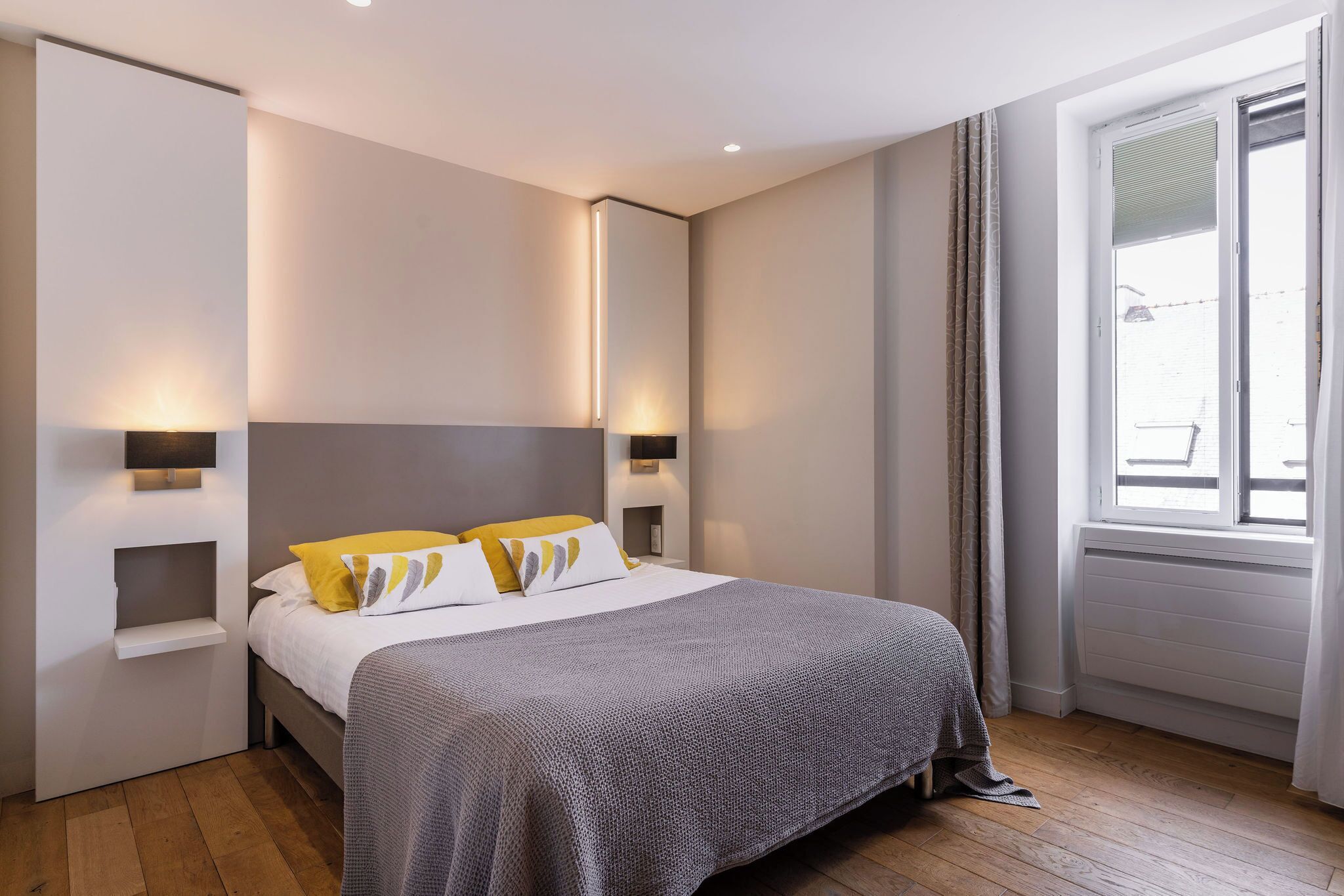 Un dormitorio moderno con una cama grande, lámparas de noche y una ventana con cortinas.