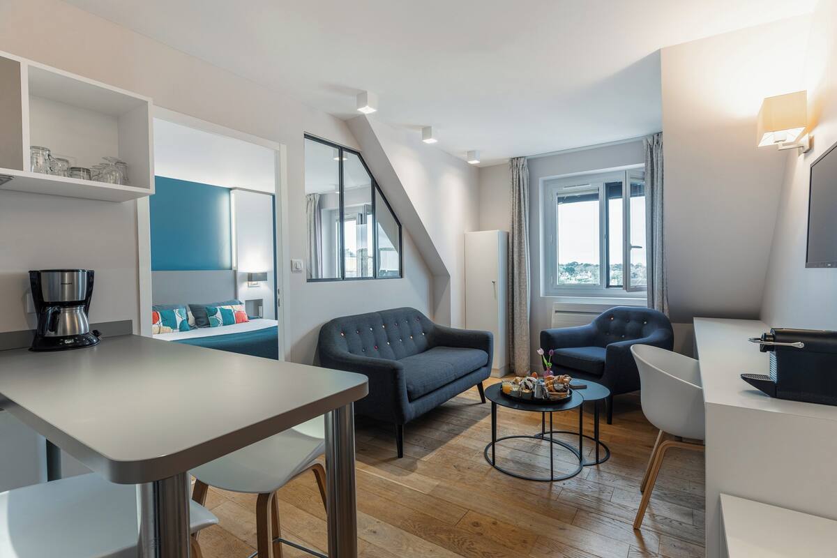 A modern, well-lit living area with a sofa, chairs, a coffee machine, and a dining table.