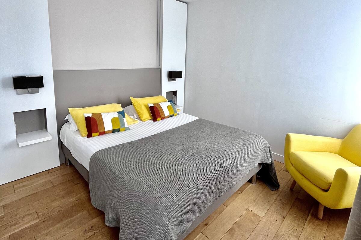A modern bedroom with a bed, a chair, and a small shelf unit.