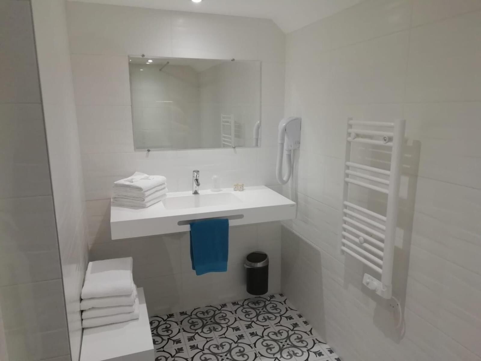 Un baño con lavamanos blanco, espejo y toallero. El piso tiene un diseño y hay un radiador blanco.