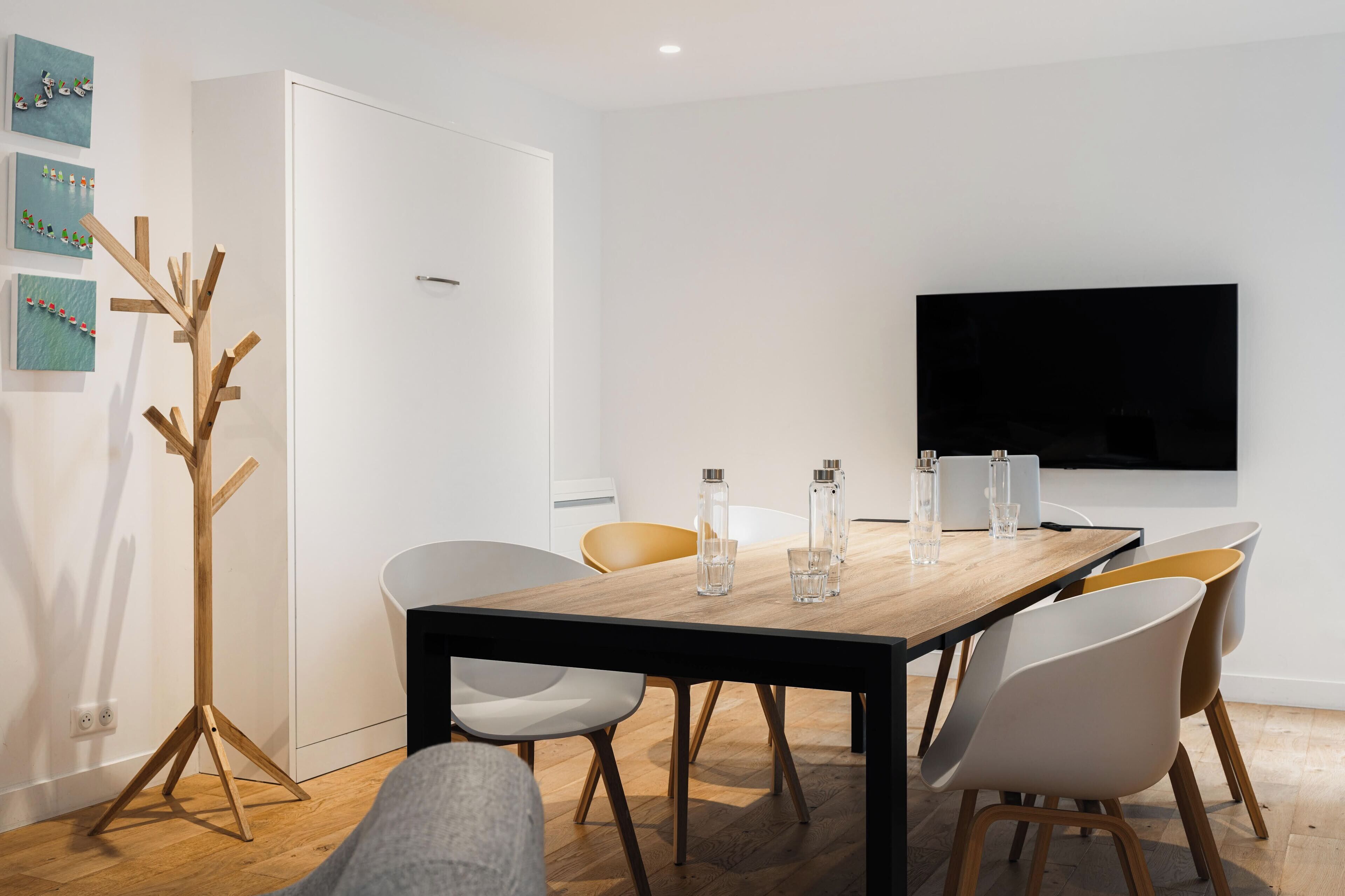 A modern dining area with a wooden table, white chairs, and a flat-screen TV mounted on the wall.