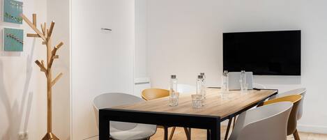 A modern dining area with a wooden table, white chairs, and a flat-screen TV mounted on the wall.