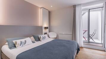 A modern bedroom with a large bed, a bedside table, a chair, and a sliding glass door leading to a balcony.