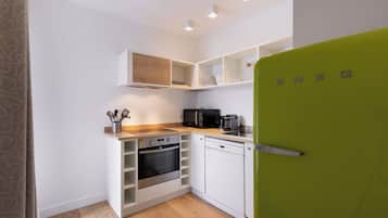 A compact kitchen with white cabinetry, a green refrigerator, and a microwave.