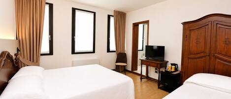 Una habitación de hotel con dos camas, televisión, escritorio con lámpara y armario.