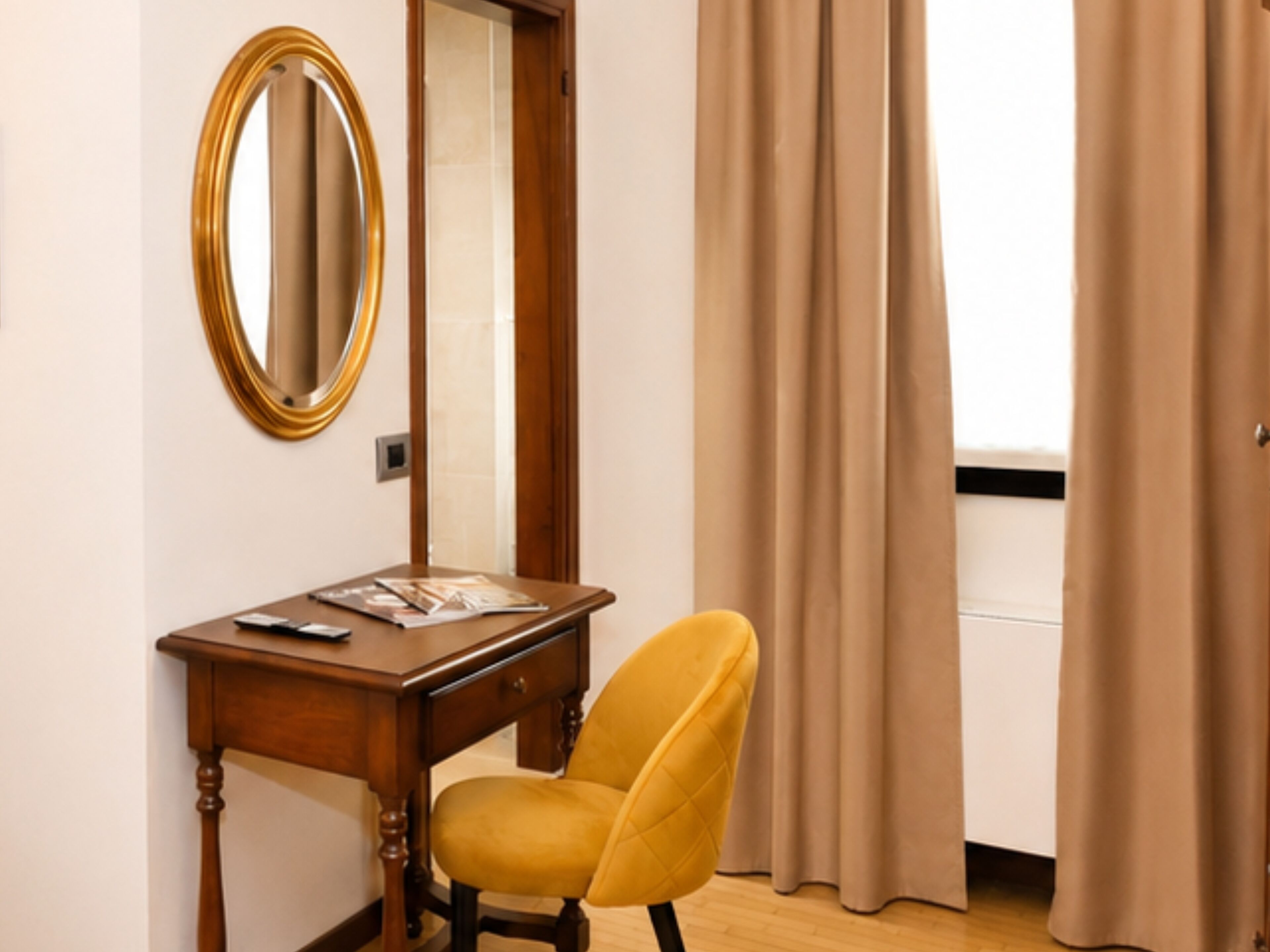 A room with a wooden desk, a chair, a mirror, and a window with curtains.