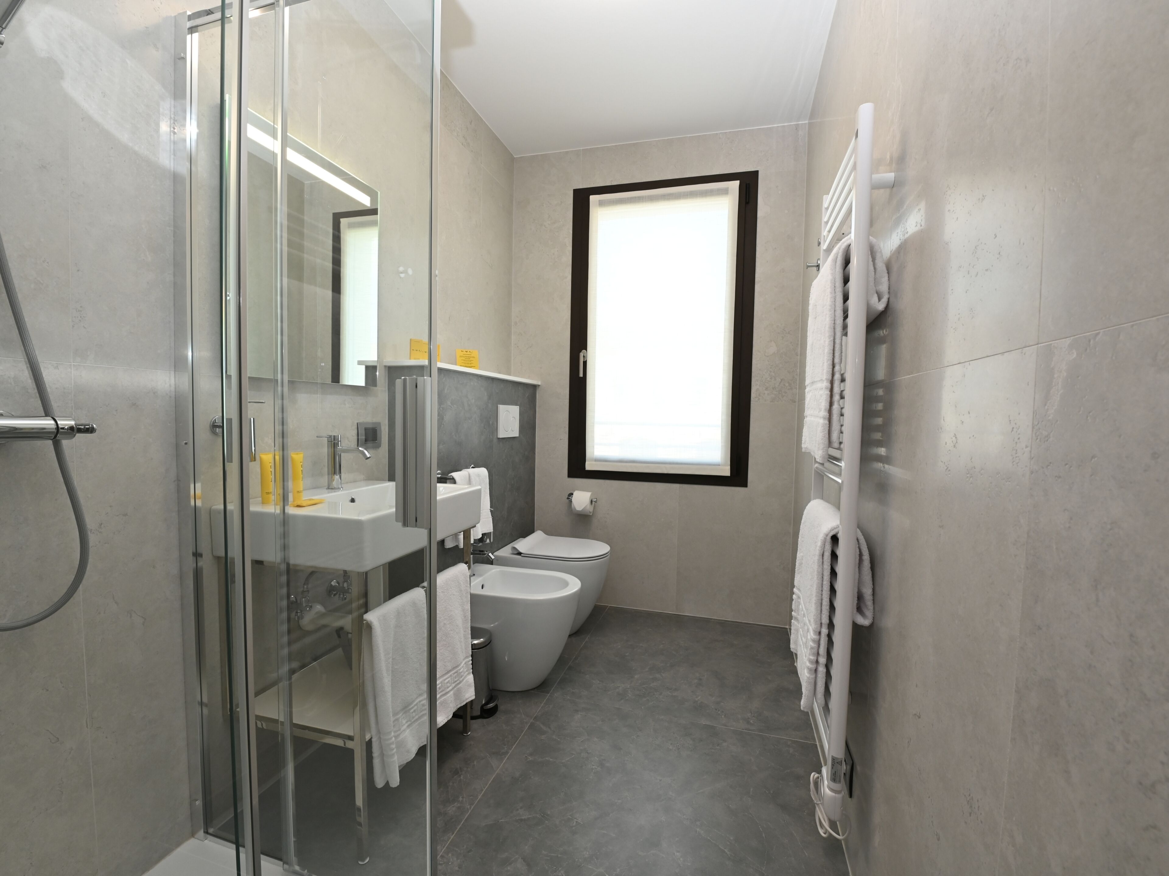 A modern bathroom with a glass shower enclosure, a sink, a toilet, and a towel rack.