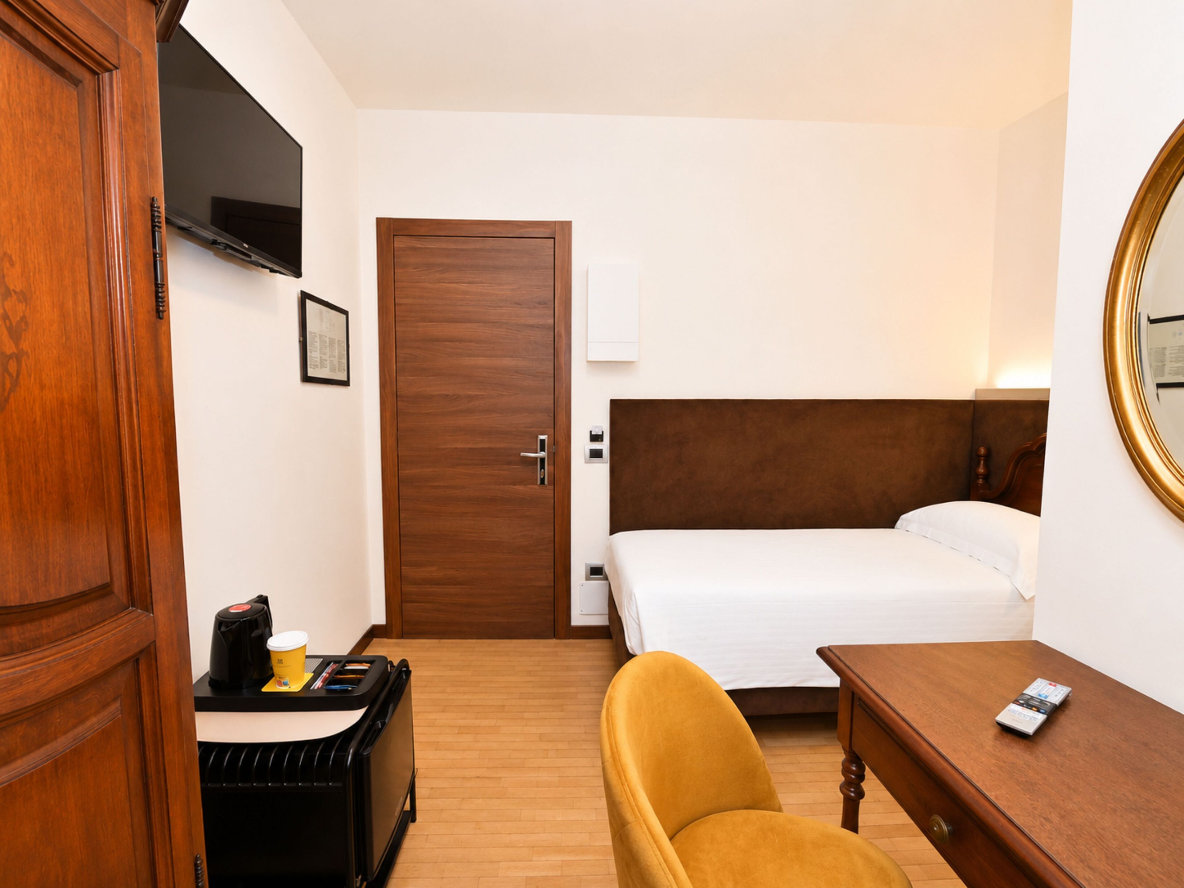 Une chambre d’hôtel comprenant un lit, un bureau avec une machine à café, une chaise et une armoire en bois.