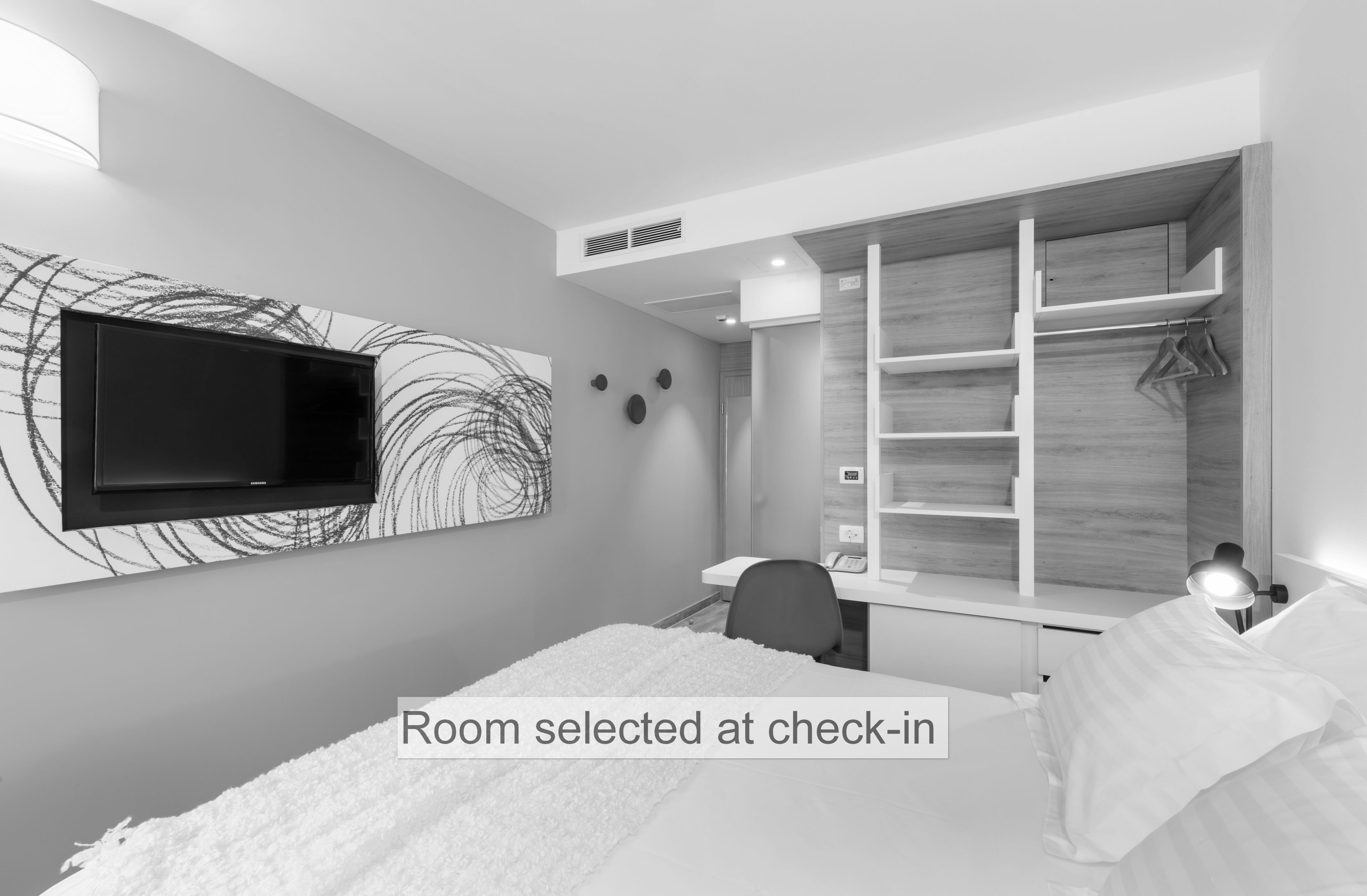 A modern bedroom with a bed, a desk, and a TV mounted on the wall.