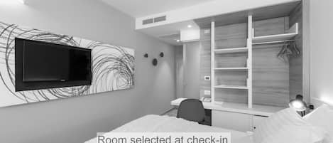 A modern bedroom with a bed, a desk, and a TV mounted on the wall.