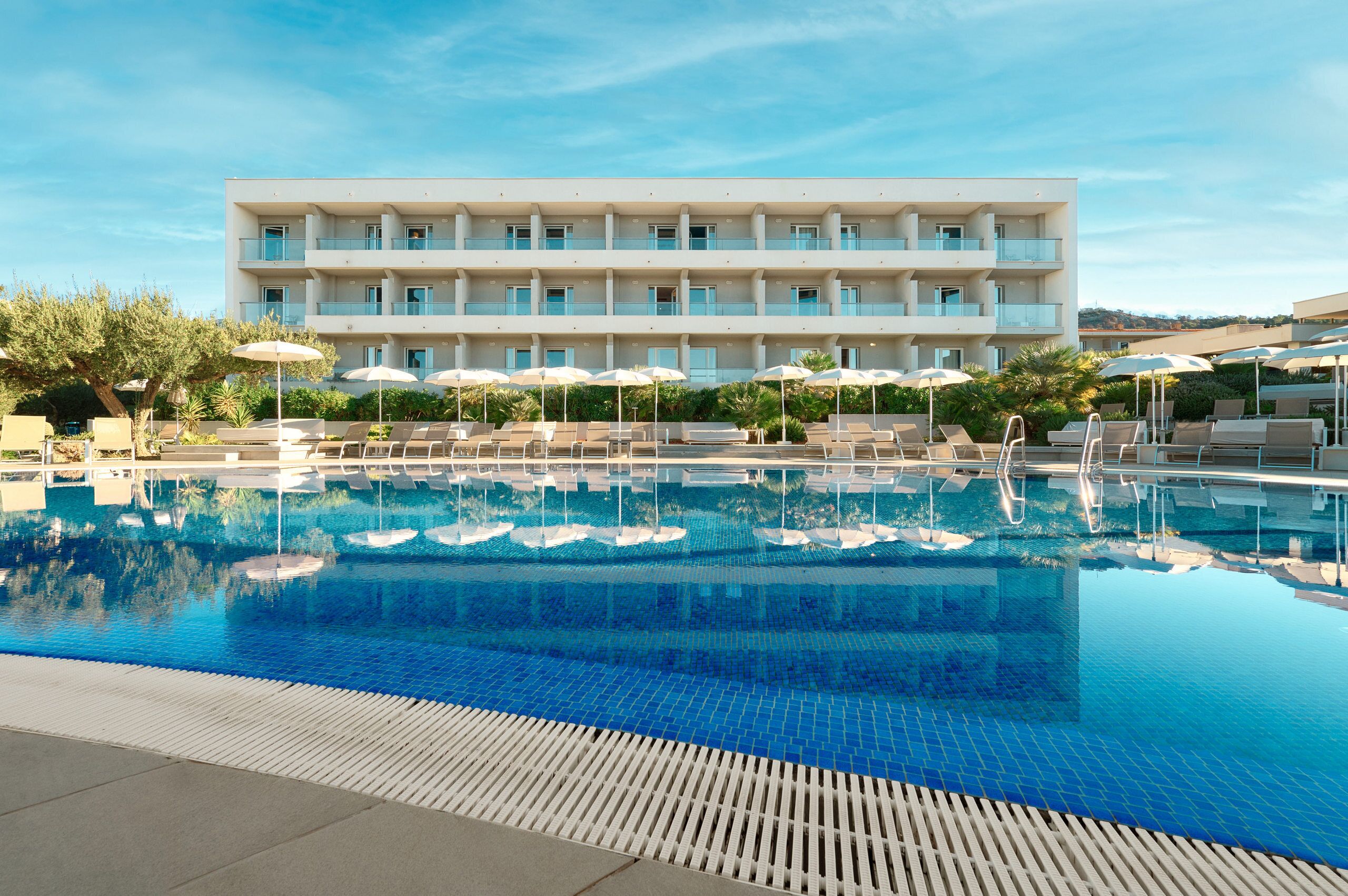 A hotel with a swimming pool, sun loungers, and umbrellas.