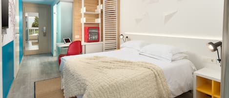 A modern hotel room with a bed, bedside table, and a desk with a computer.
