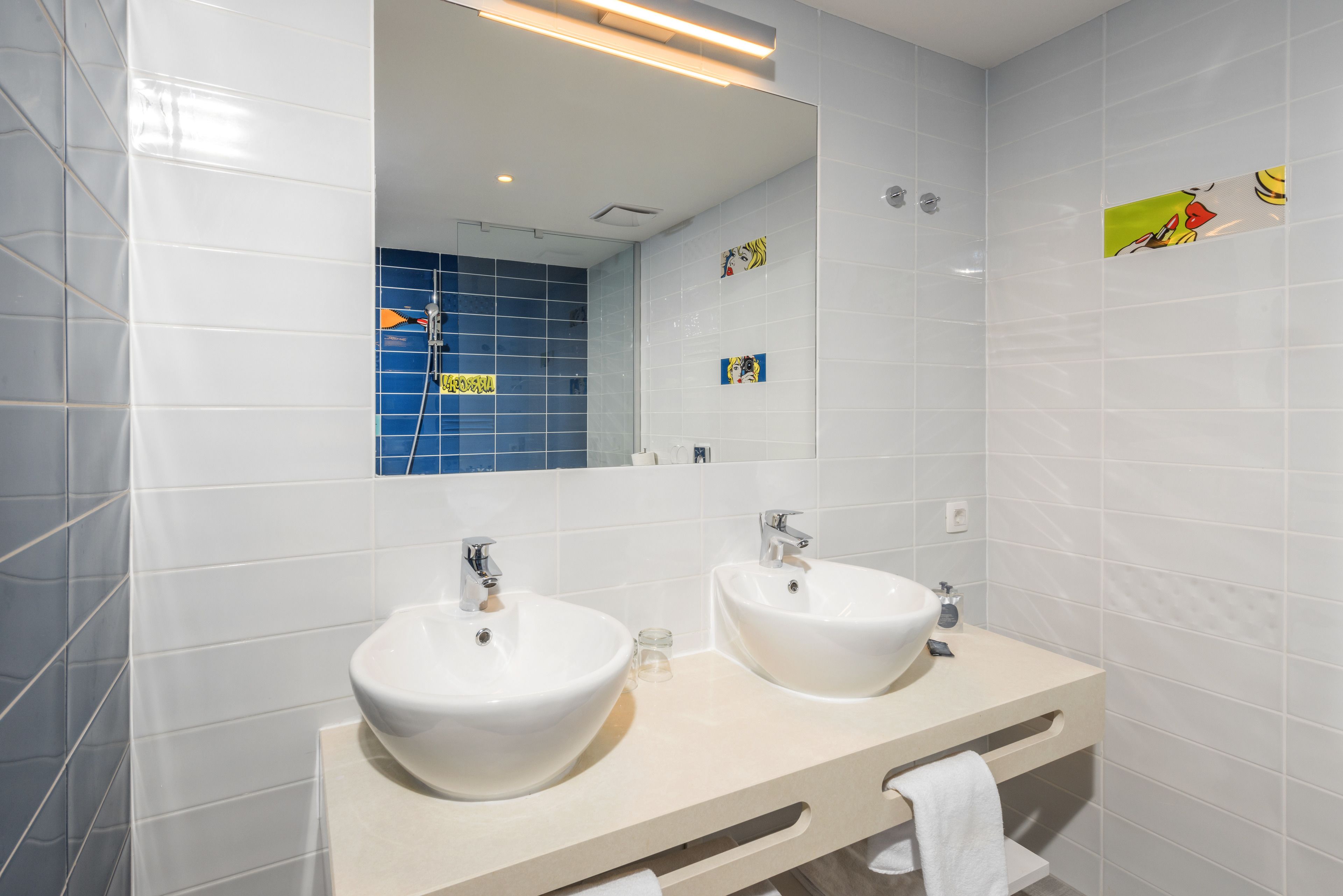 A modern bathroom with two sinks, a large mirror, and blue-tiled shower area.
