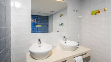 A modern bathroom with two sinks, a large mirror, and blue-tiled shower area.