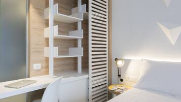 Ein modernes Schlafzimmer mit weißem Schreibtisch, einem Sessel, einem Bett mit weißer Bettwäsche, einem Nachttisch mit Lampe und einer eingebauten Regaleinheit.