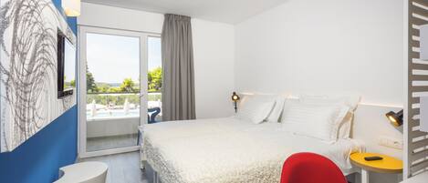 Habitación de hotel moderna con una cama grande, una silla roja, una mesita pequeña y vistas al exterior.
