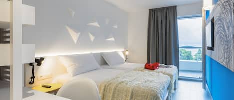 A modern hotel room with a bed, a desk with a laptop, and a view of the outdoors.