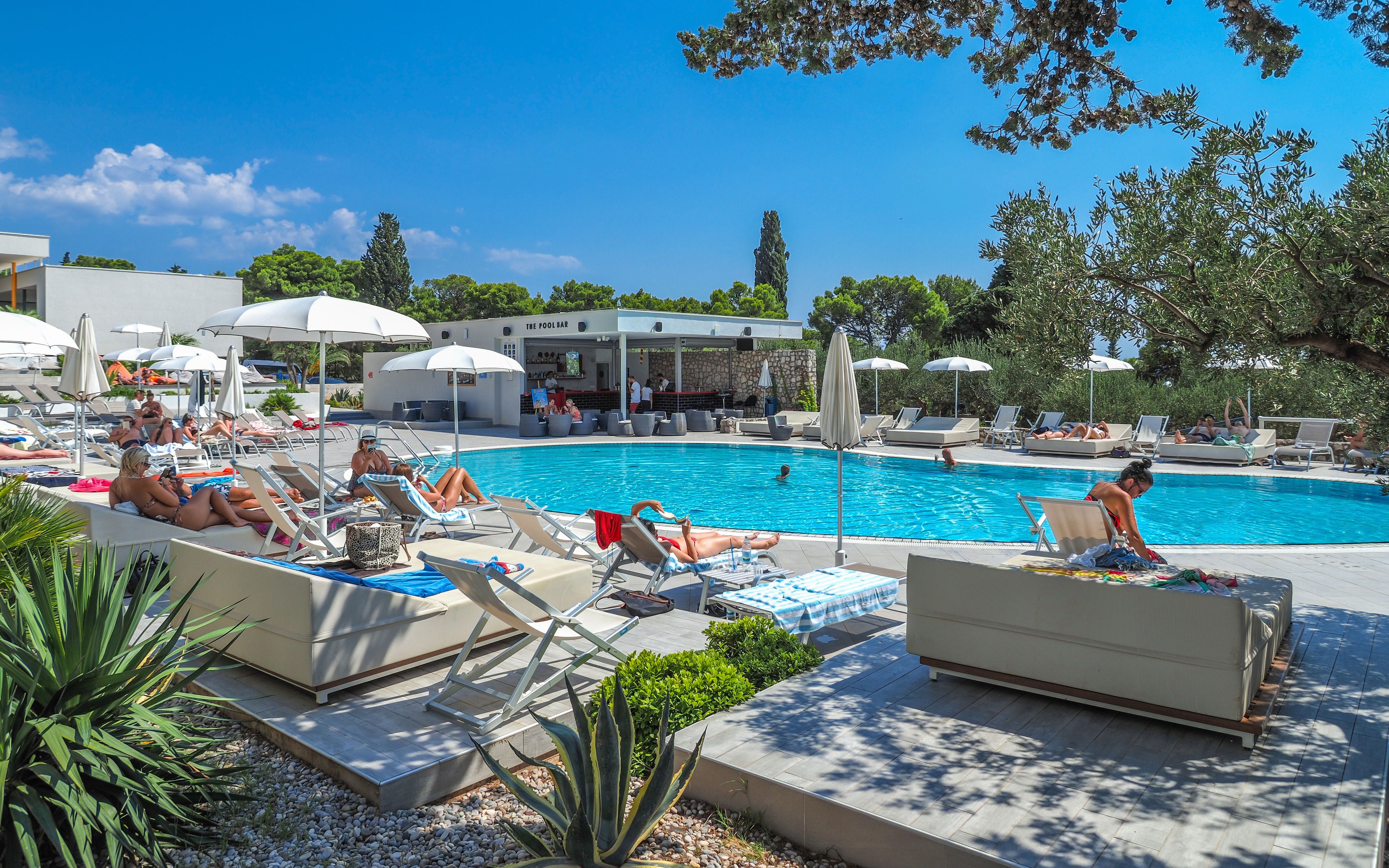Ein Poolbereich mit Liegestühlen, Sonnenschirmen und einer Bar.