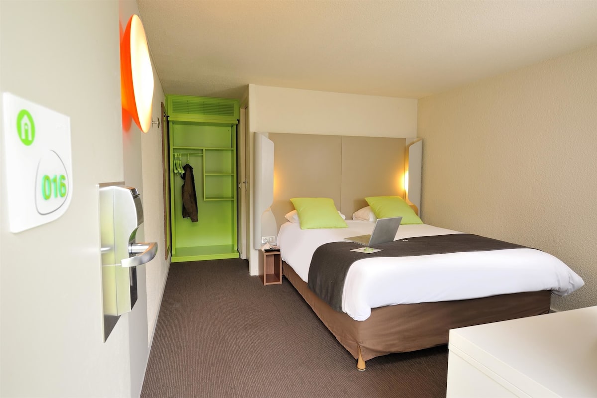 Ein Hotelzimmer mit Bett, Nachttisch und einer grünen Tür zu einem Schrank.