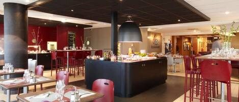 Un restaurante moderno con sillas y mesas rojas, una isla central con comida, y un techo negro.