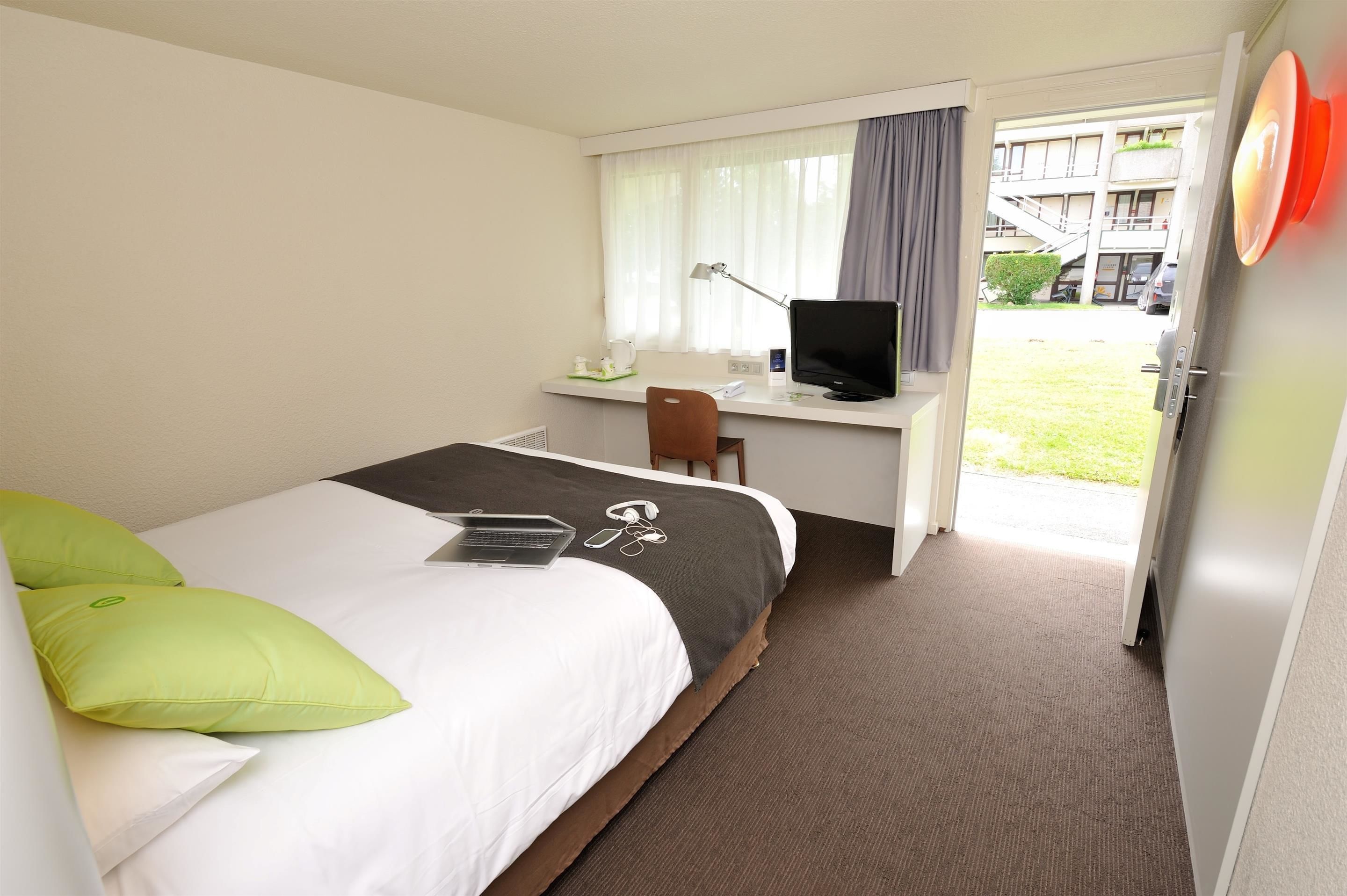 A hotel room with a bed, a desk with a computer, and a view of the outside.