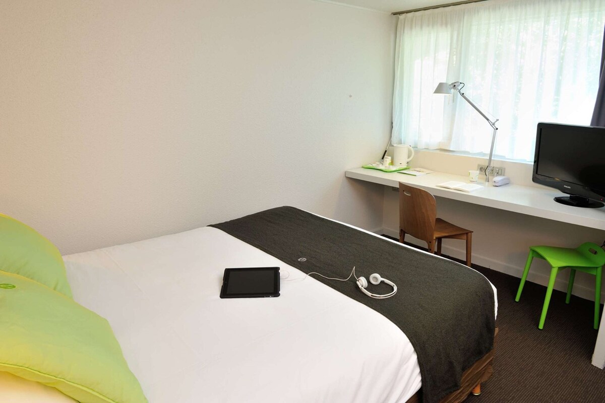 A hotel room with a bed, a desk, a chair, a television, and a window with curtains.