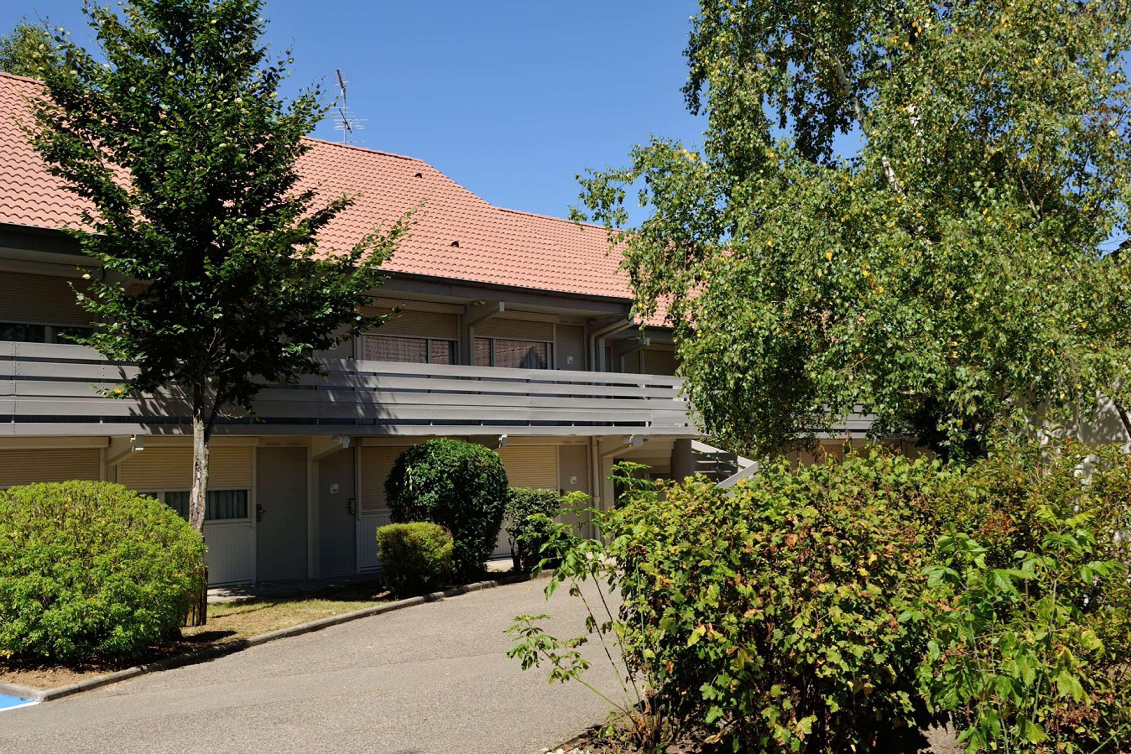 Un motel à deux étages, avec un toit recouvert de tuiles rouges, un espace de stationnement couvert et une pelouse bien entretenue.