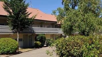 Un motel à deux étages, avec un toit recouvert de tuiles rouges, un espace de stationnement couvert et une pelouse bien entretenue.