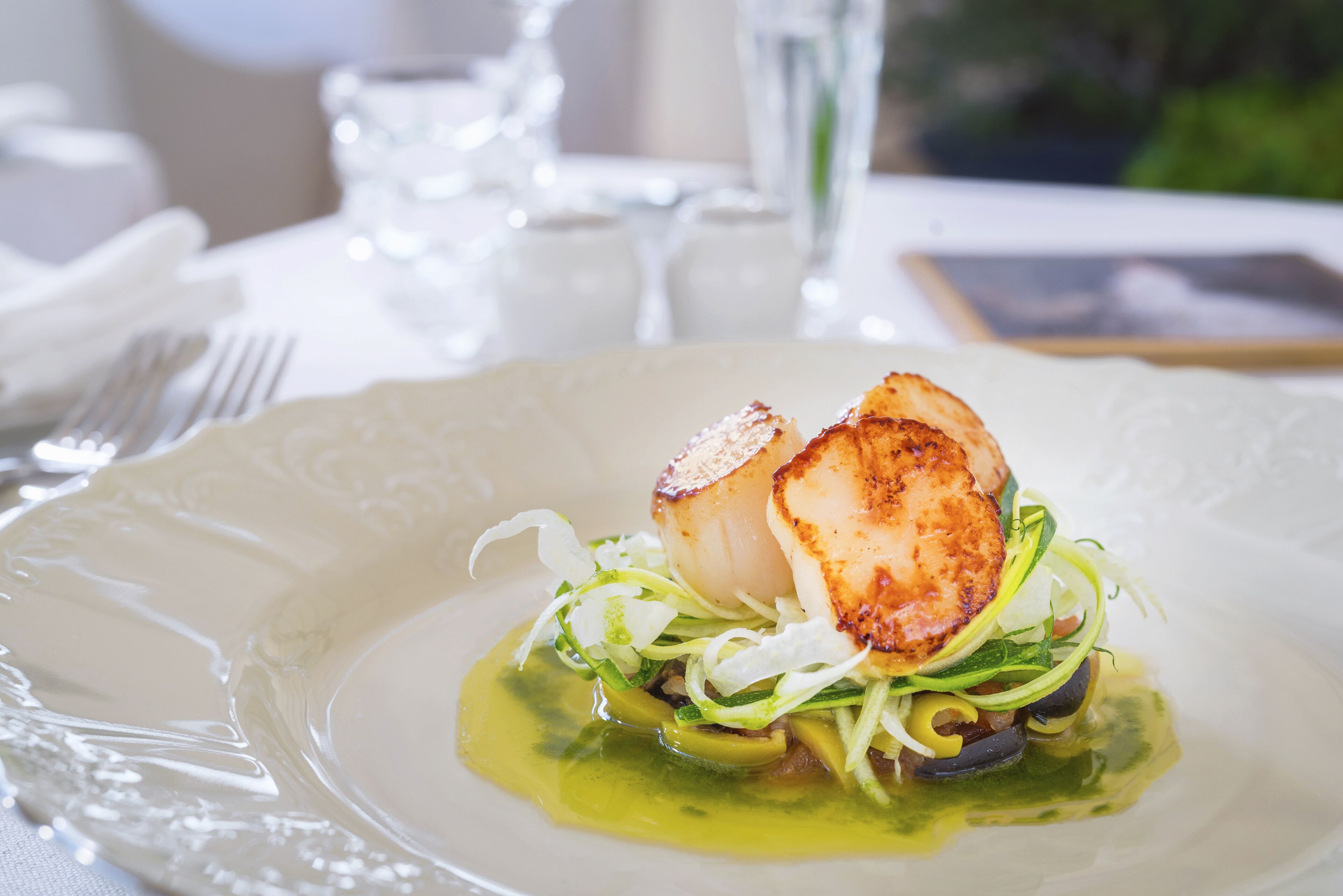 A plate of seared scallops with greens and a light dressing.