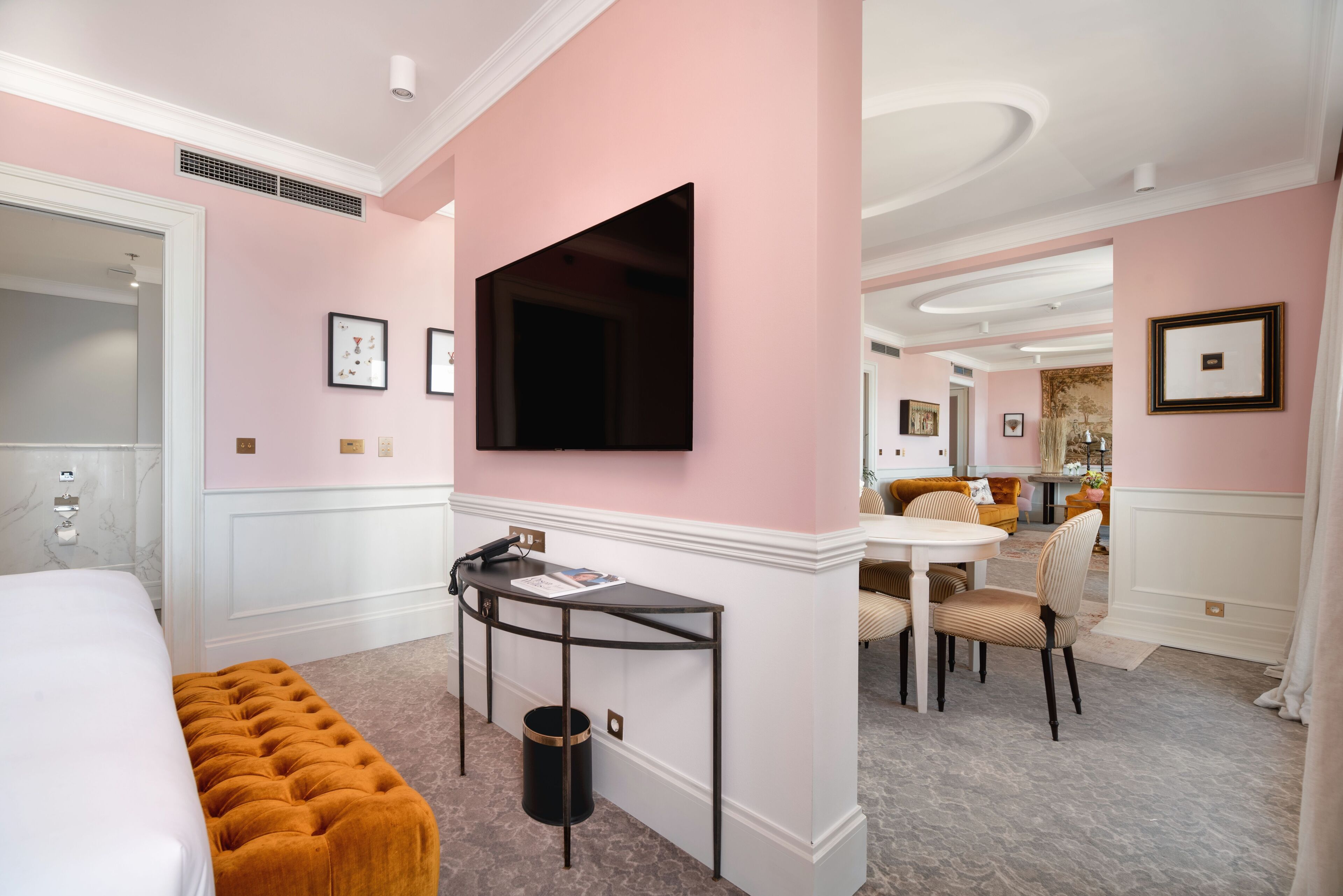 A hotel room with a bed, a desk, a chair, a television, and a dining area with a table and chairs.