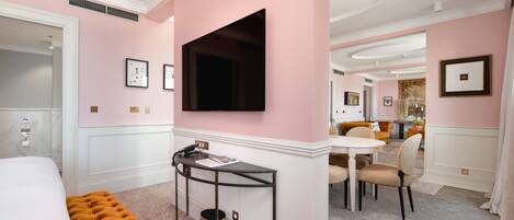 A hotel room with a bed, a desk, a chair, a television, and a dining area with a table and chairs.