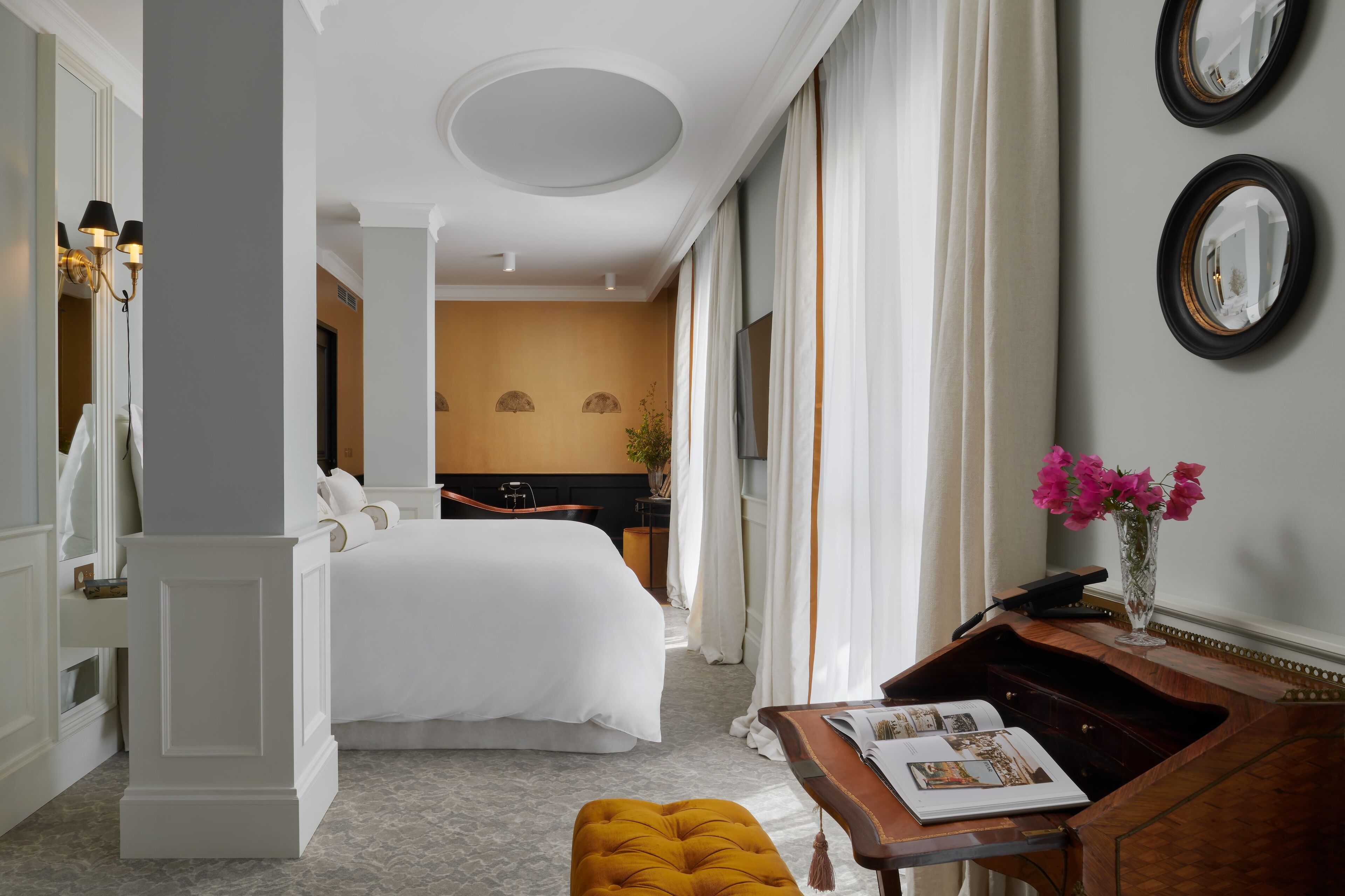 A hotel room with a large bed, a desk with a vase of flowers, and a view of the bathroom.