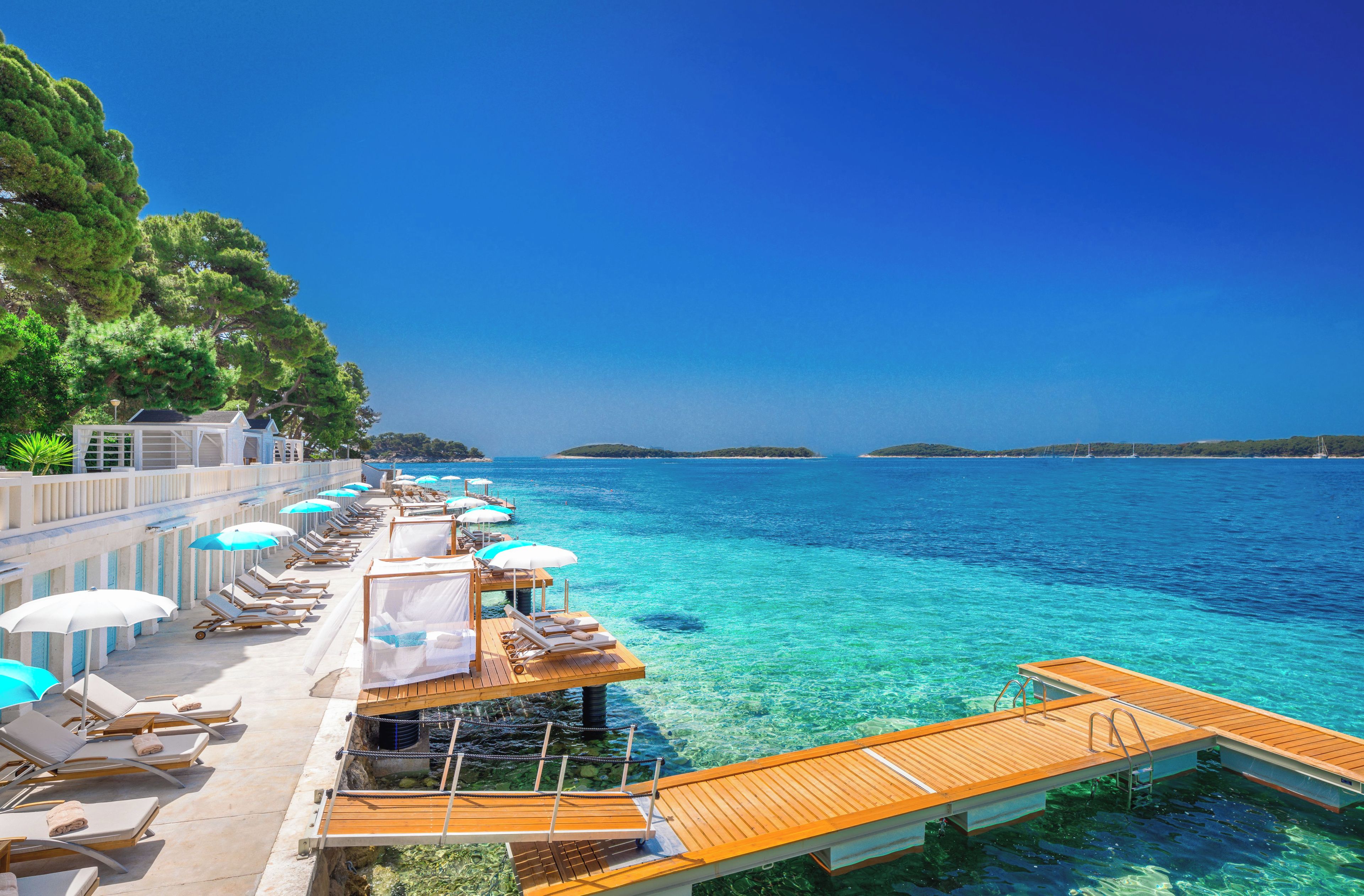 A seaside resort with clear blue waters, wooden deck loungers, and umbrellas.