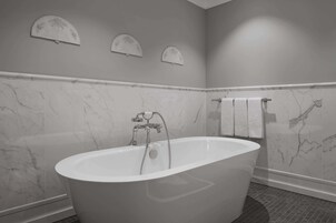 Un baño moderno con una bañera independiente, paredes de mármol y suelo de baldosas.