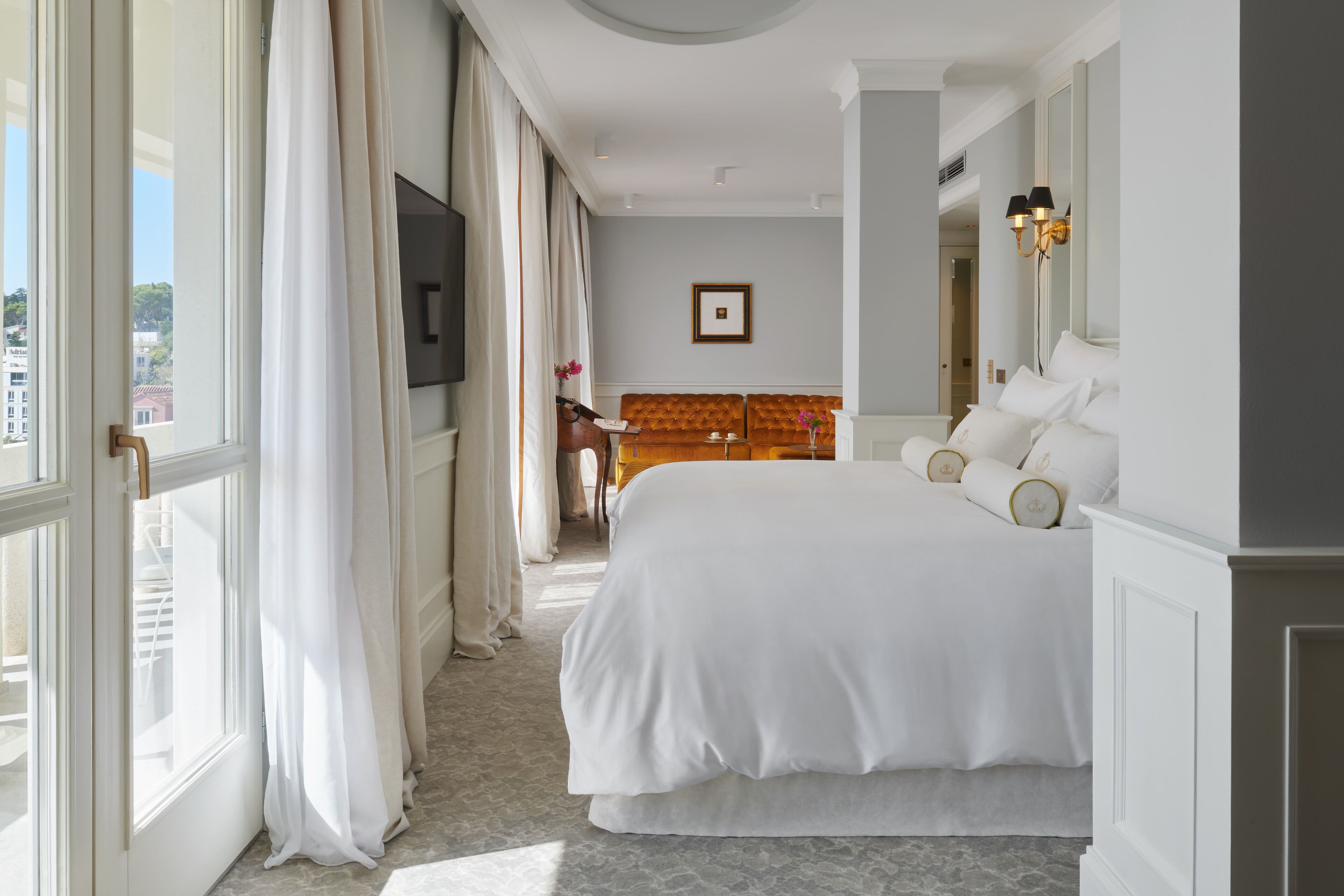 A hotel room with a large bed, a television, a framed picture on the wall, and a view of the city through the window.