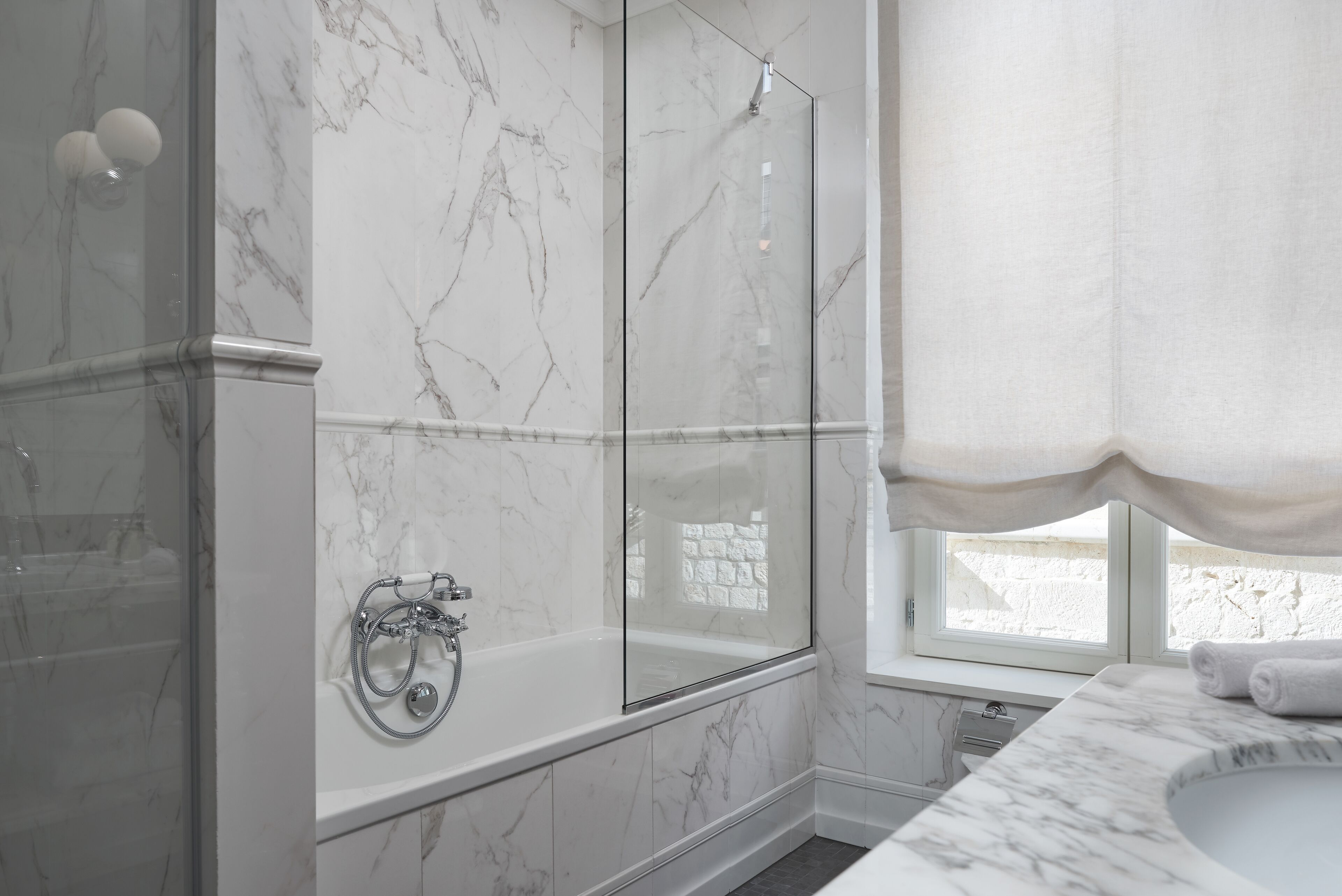 A modern bathroom with a glass-enclosed shower, a freestanding bathtub, and a marble-topped sink.