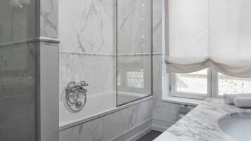 A modern bathroom with a glass-enclosed shower, a freestanding bathtub, and a marble-topped sink.