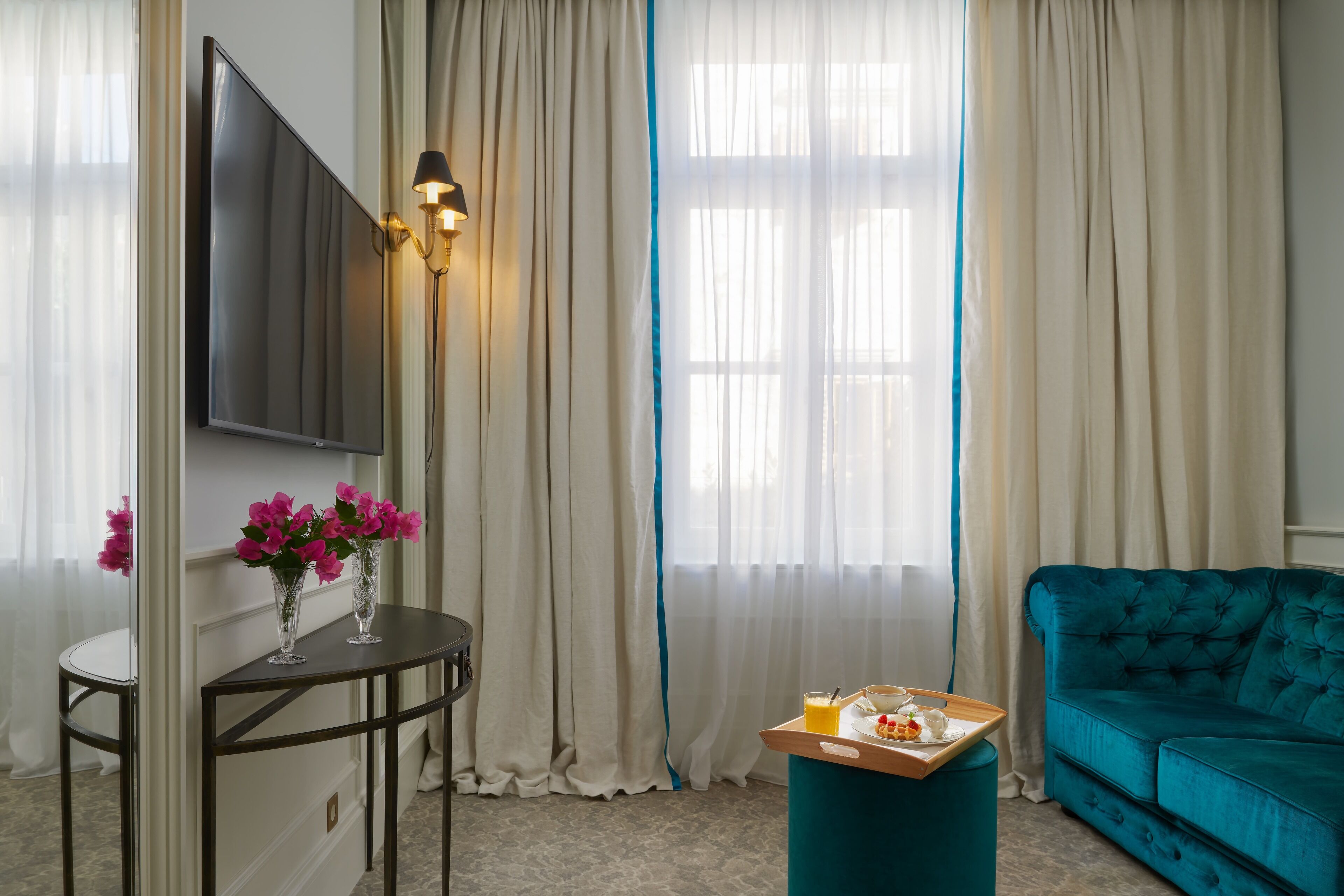 Un saló modern amb un sofà color turquesa, un televisor de pantalla plana penjat a la paret, una taula rodona amb un ram de flors i un servei de petit esmorzar a terra.