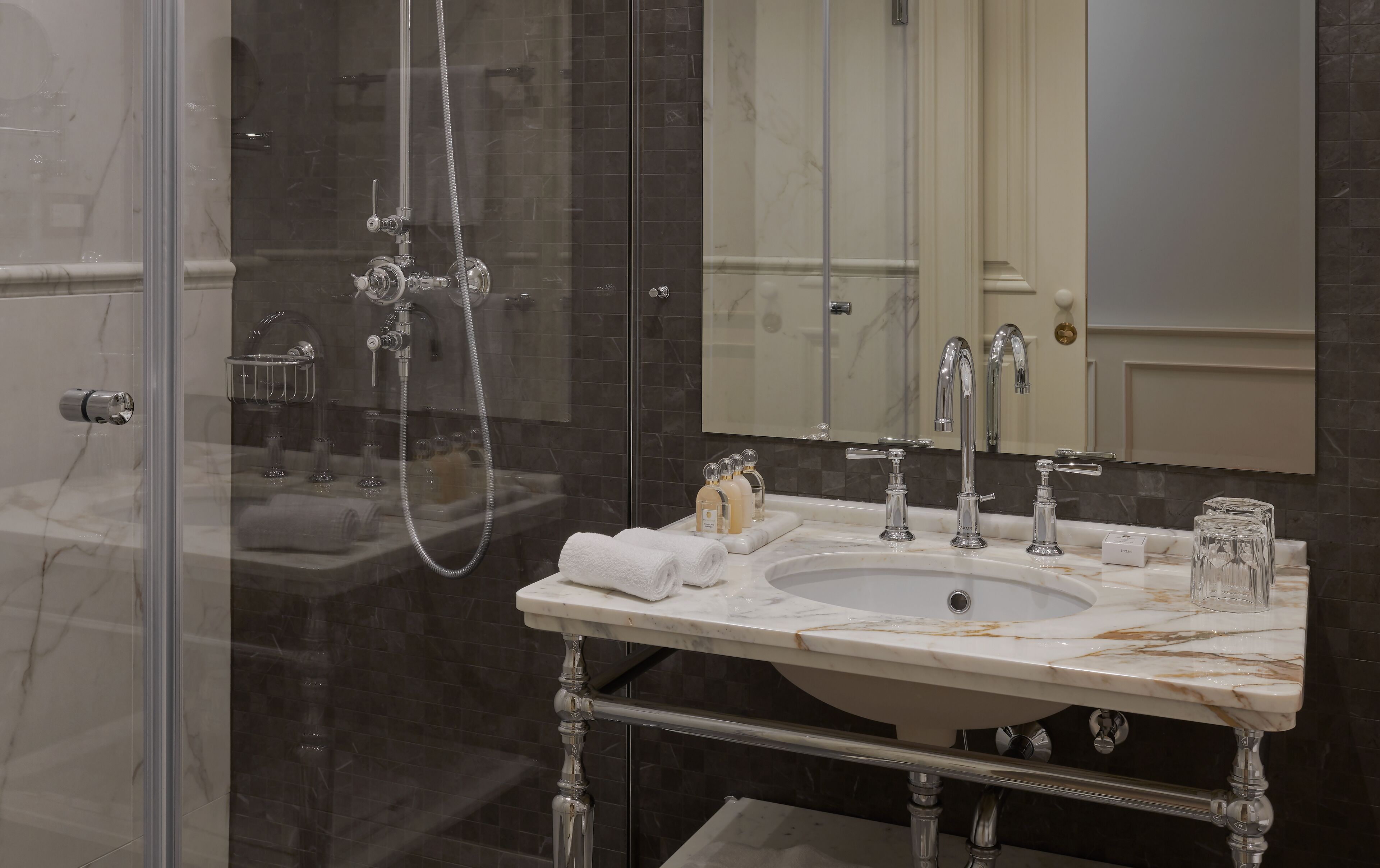 A bathroom with a glass-enclosed shower, a marble sink, and a large mirror above the sink.