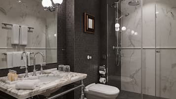 A modern bathroom with a marble sink, two faucets, a toilet, and a glass-enclosed shower.