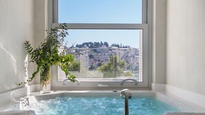 A bathroom with a bathtub, a window, and a view of a cityscape. - Adriana Hvar Spa Hotel (Hvar)