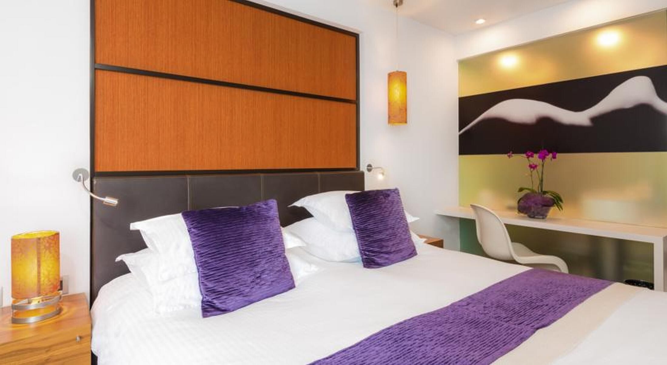 Una habitación de hotel moderna con una cama grande, un escritorio y un televisor montado en la pared.