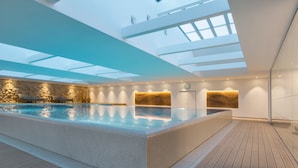 A modern indoor swimming pool with a skylight ceiling, stone wall, and wooden deck. - Adriana Hvar Spa Hotel (Hvar)