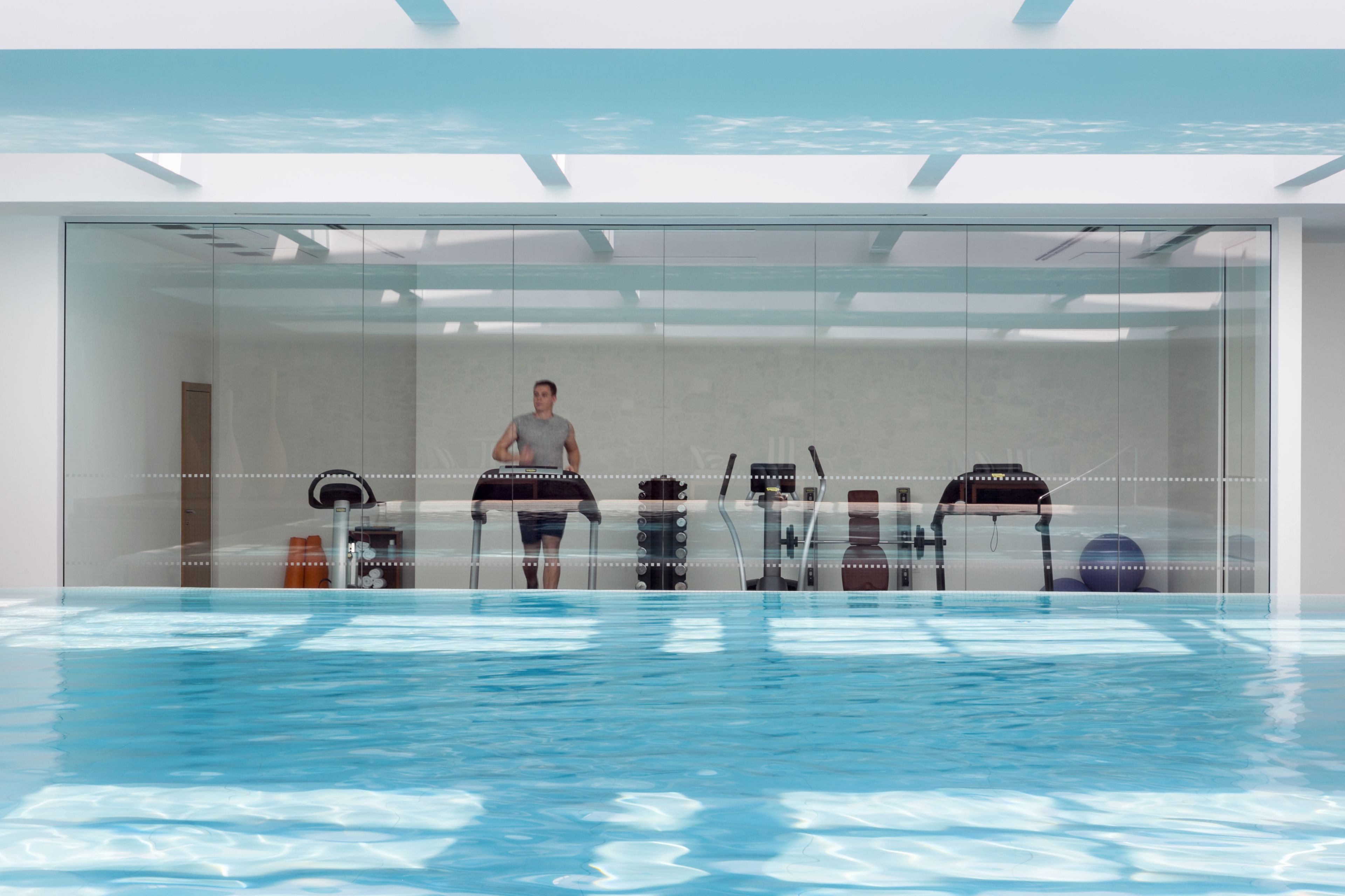 Ein Schwimmbecken mit einer Person, die auf einem Gerät trainiert, umgeben von Glaswänden und einer transparenten Decke.